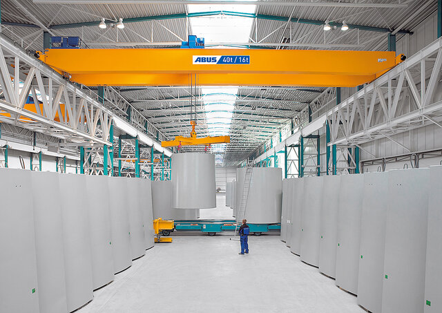 Una gru a ponte in un capannone industriale movimenta carichi pesanti, mentre un operaio si trova nell'area di lavoro.