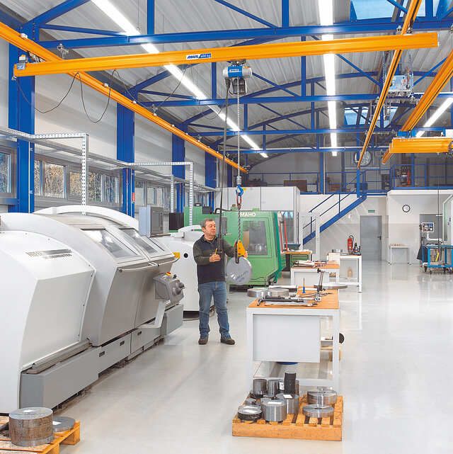 Un addetto aziona un sistema a vie di corsa sospese con paranco a catena e sposta un carico all'interno di un capannone