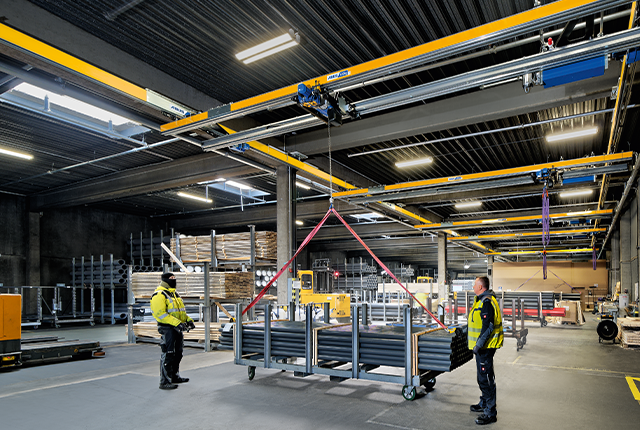 Il carroponte bitrave ZHB effettua il sollevamento di un carico all'interno di un capannone industriale, mentre i dipendenti assistono all'operazione.