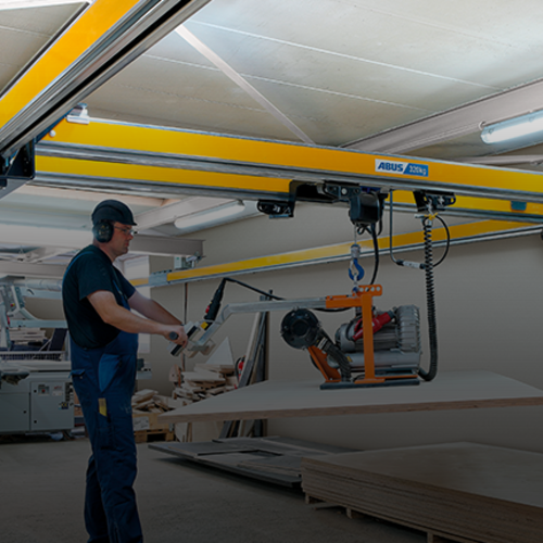 Un operatore aziona una gru bitrave ZHB-X e effettua il sollevamento di un carico con un paranco a catena all'interno di un capannone.