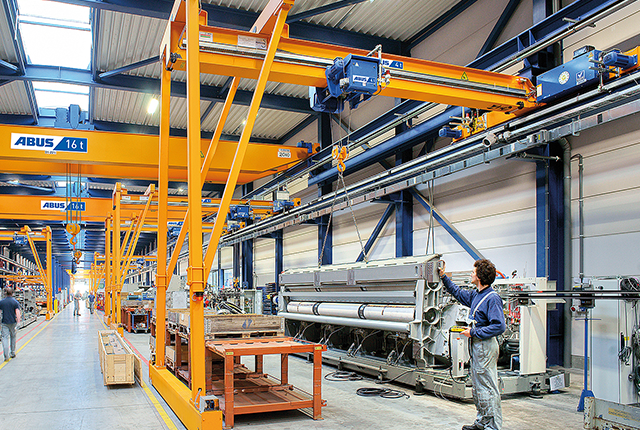 Gru a semiportale ABUS in un capannone industriale con portata fino a 10 t e luce fino a 15 m per la movimentazione flessibile dei materiali nelle postazioni di lavoro.