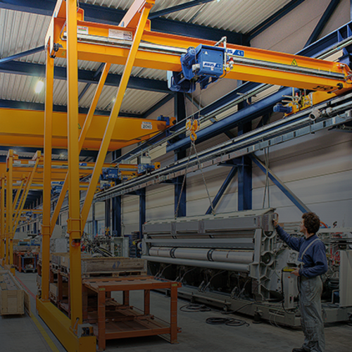 Gru a semiportale ABUS in un capannone industriale con portata fino a 10 t e luce fino a 15 m per la movimentazione flessibile dei materiali nelle postazioni di lavoro.